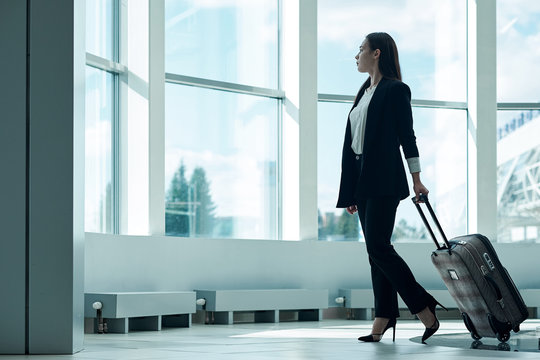 Young asian business woman in airport with baggage trolley bag, waiting for departure