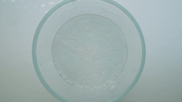 Zoom in top view shot of hand throwing effervescent tablet into glass of water. Pill falling down, making splash and dissolving with bubbles on white background