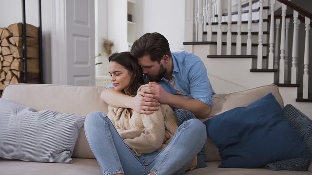 Front view of despleased upset young woman which breaking out of the husband's embrace after he trying to make peace with her after the altercation