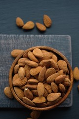 Almonds nuts close-up in a wooden spoon on a wooden brown scratched background.Raw almonds in a round wooden cup on a black slate background.Vegetarian and vegan food.Healthy food.
