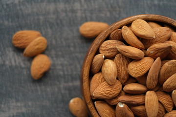 Almonds nuts close-up  on a wooden brown scratched background.Raw almonds in a round wooden cup on a black slate background.Vegetarian and vegan food.Healthy food.