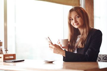 Young business woman using her smart phone and smiling in coffee shop