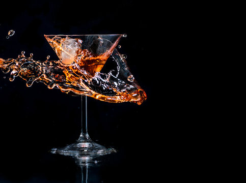 Cocktail splash in martini glass over black background with copyspace. Alcohol drink menu design.