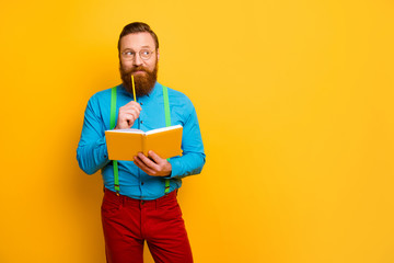 Photo of handsome business guy hold planner creative idea new project look empty space thinking wear bright blue shirt green suspenders red pants isolated yellow color background