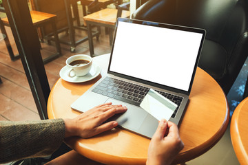 Mockup image of a woman holding credit card while using laptop with blank white screen and coffee cup on wooden table