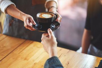 A waitress holding and serving a cup of hot coffee to a male customer in cafe