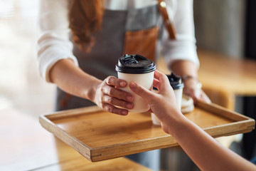 A waitress holding and serving paper cups of hot coffee to customer in cafe