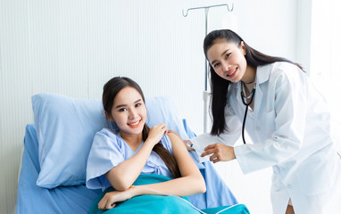 Asian young female doctor with syringe to the arm of Asian young female patient on Bed for better healing In the room hospital background.