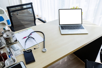 laptop computer with a blank white screen with stethoscope,vial,syringe,empty paper clipboard and medical bottle different drugs on surgical tray with medical equipment on wooden table background