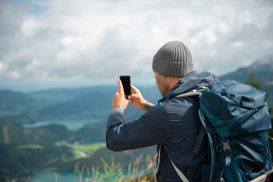 Man with backpack  taking a photo of scenic view in mountains
