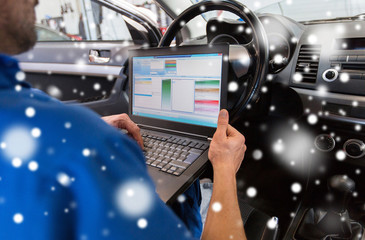 car service, repair, maintenance and people concept - mechanic man with laptop computer making system diagnostics at workshop over snow