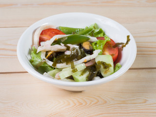 Seafood and vegetables salad. Salad in a round white plate on a wooden surface. View from above