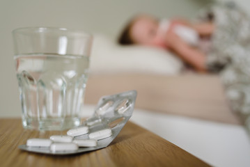 Sick child lying in bed with pills and glass of water