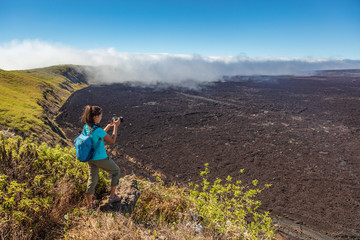 Galapagos tourist hiking on volcano Sierra Negra on Isabela Island taking photos with camera. Woman...
