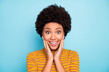 Fototapeta na wymiar Photo of beautiful pretty dark skin curly lady listen amazing good news open mouth unexpected emotions arms on cheekbones wear yellow striped shirt isolated blue color background