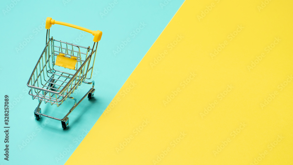 Wall mural empty miniature shopping cart on blue and yellow background. toy trolley on bright colorful backgrou