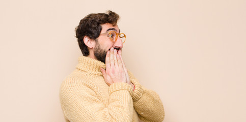 young cool man looking happy, cheerful, lucky and surprised covering mouth with both hands against...