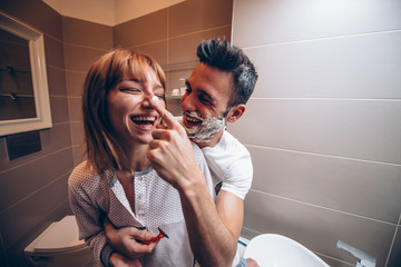 Beautiful young couple of lovers in the bathroom having fun playing with shaving foam.