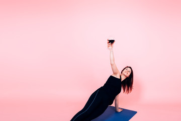 young woman holding a glass of red wine while performing yoga - wine and yoga trend concept