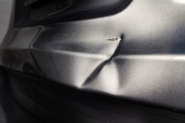 A dent in the body of a silver car in exciting light.