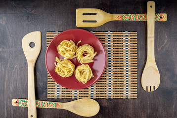 four fettuccine on a red ceramic plate on a bamboo napkin surrounded by bamboo blades on a dark wooden background