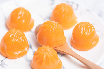 A bun like an orange in a white plate on the table