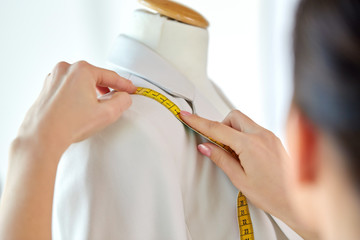 tailoring, sewing and clothing concept - close up of fashion designer measures jacket with tape measure