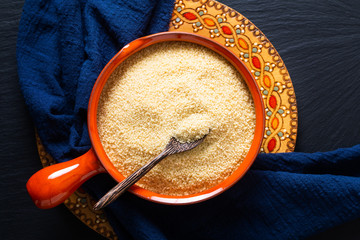 Food concept organic raw couscous in orange bowl on blask slate stone board with copy space © TYSB