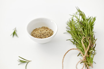 Fototapeta na wymiar greens, culinary and flavoring concept - bunch of fresh rosemary herb and dry seasoning in cup on white background