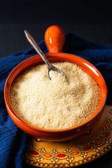 Food concept organic raw couscous in orange bowl on blask slate stone board with copy space © TYSB