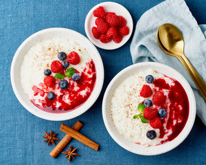 Rice pudding. French milk rice dessert with raspberries, blueberries. Blue linen textile. Top view
