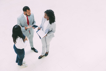 Diverse business colleagues discussing work issues in office hallway. Business man and women standing in circle, holding tablet and papers and talking. Corporate meeting concept