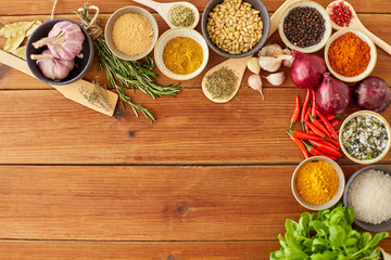 food, culinary and eating concept - bowls with different spices, onion, garlic with pine nuts and red hot chili pepper on wooden table