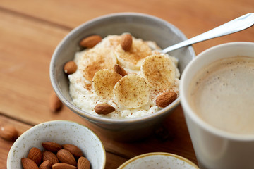 food and breakfast concept - oatmeal porridge in bowl with sliced banana, almond nuts and cinnamon and cup of coffee on wooden table