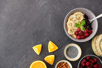 food and breakfast concept - oatmeal cereals in bowl with wild berries, fruits, almond nuts and poppy seeds on slate stone table