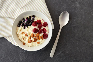 food and breakfast concept - porridge in bowl with wild berries, almond nuts and spoon on slate stone table
