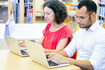 Serious adult students taking exam in classroom. Man and woman in casual sitting at desk, using laptops, typing, looking at monitor. Taking tests concept