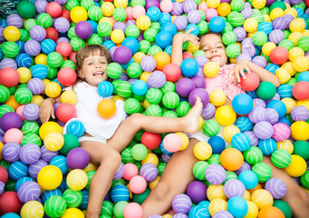Fototapeta na wymiar Two girls playing in pool with colorful plastic balls in game room. Child looking at camera