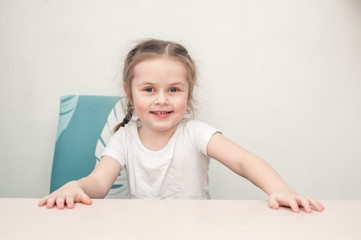 Little girl sitting at table and smiling to the camera.