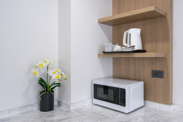 Microwave cooking machine on white marble counter with electric kettle on wooden cabinet interior...