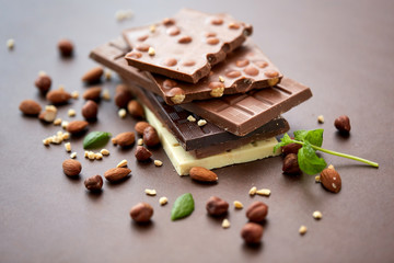 sweets, confectionery and food concept - bars of dark, white and milk chocolate with nuts on brown background