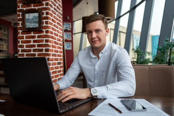Young businessman wearing a white stylish shirt sitting at a cafe working on a laptop. Freelance and modern business concept. Distance job, selfemployed.