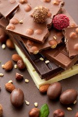sweets, confectionery and food concept - close up of different chocolate bars, candies and nuts on brown background