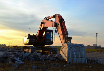 Large tracked excavator on a construction site on the awesome sunset background. Road repair,...