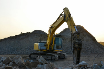 Large tracked excavator with hydraulic hammer breaks asphalt at a construction site on the background sunset. Breaking rock and reinforced Concrete. Road repair, asphalt replacement. Demolition tools