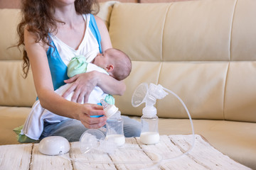 A young mother breastfeeds her baby and an electric breast pump is standing in front of her on a...