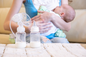 A young mother breastfeeds her baby and an electric breast pump is standing in front of her on a table