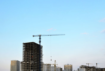 Fototapeta na wymiar Tower crane and new residential high-rise buildings at a huge construction site on sunset background. Building construction, installation of formwork and concrete structures
