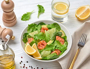 Salmon salad, cucumber, spinach, lollo, lettuce. Home made vegetarian salmon salad. Seafood tasty diet concept. Mix leaves greens with salmon fish in plate on white wood background.