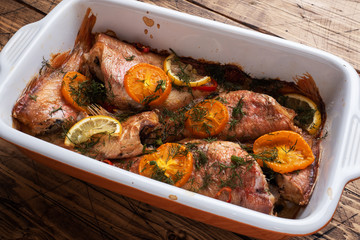 Baked sea bass with tomato pepper lemon and herbs in a ceramic baking sheet on a wooden background. Fish cooked in a home oven on the table.